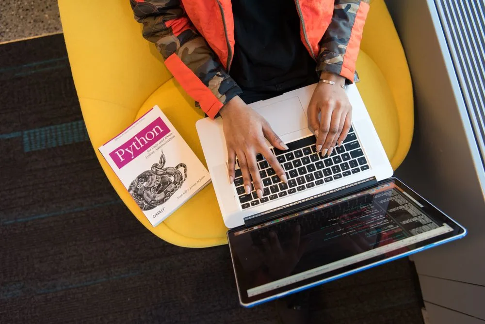 A developer working with a laptop and a programming reference book