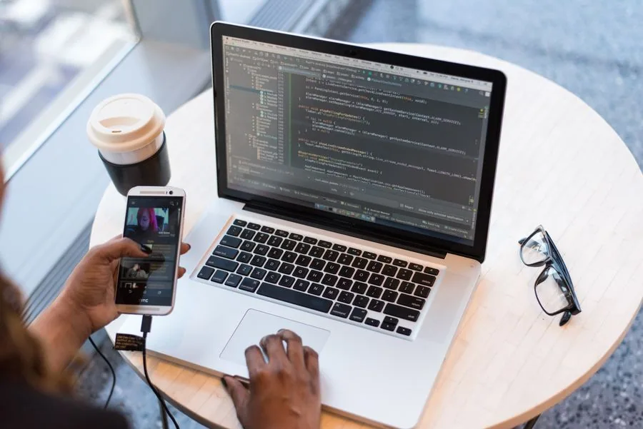 A developer using a phone beside a laptop at a desk