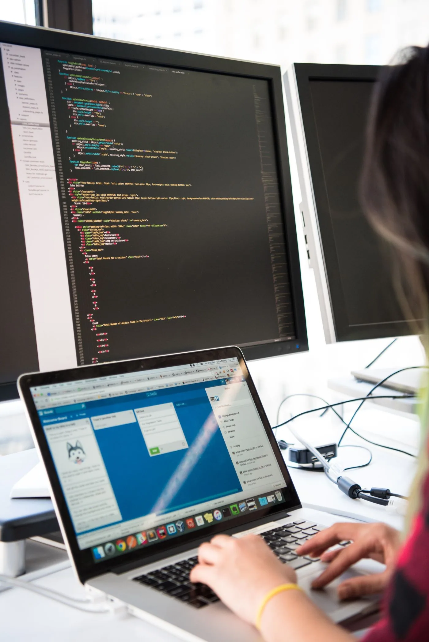A developer working across a laptop and larger code displays